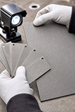 Man holding sandblasted metal texture samples for surface quality inspection. Industrial metalworking control and finish testing. Specialist examining metal plate roughness with light.
