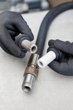 Worker replacing worn ceramic nozzle on sandblasting hose in workshop. Man hands with protective glove maintaining industrial abrasive equipment. Metal surface treatment technology.