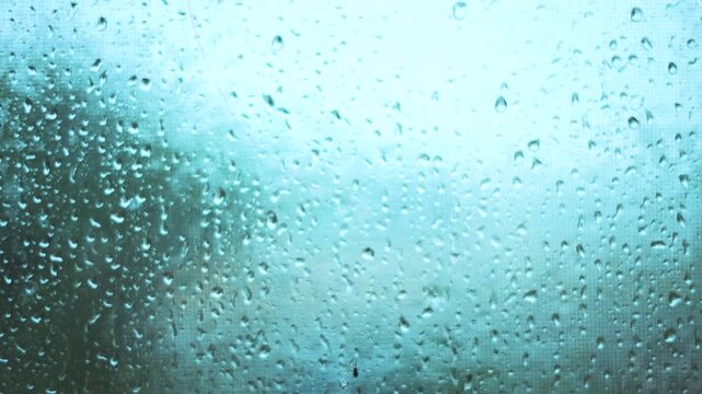 The rain creates a serene scene with droplets on the glass. The droplets blur the view outside, reflecting a calm, rainy atmosphere.