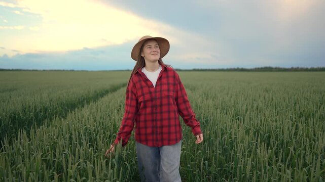 A woman in a red plaid shirt walks through a green field. The woman smiles as she strolls amid tall green crops under a soft sky.
