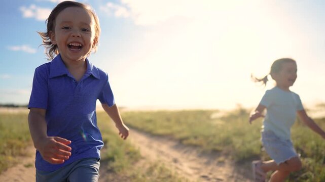 A boy and a girl run joyfully on a dirt path. The boy and girl enjoy their laughter while playing in the golden sunlight.