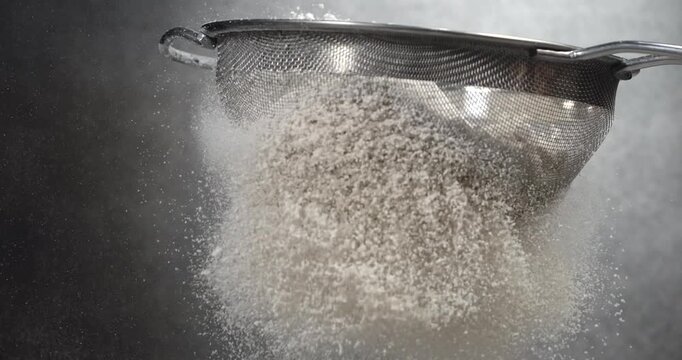 Flour sifts through a sieve creating soft powder cloud in slow motion