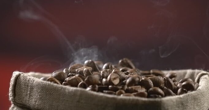 Roasted coffee beans falling into a burlap sack with rising steam in slow motion
