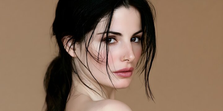 Beautiful young woman with dark hair and nose ring looking into camera against a smooth neutral solid beige studio background