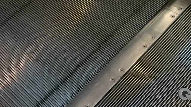 Metallic escalator steps move steadily upward. Shiny surfaces reflect ambient building lights. Industrial texture dominates the modern structure. Clean, precise lines define the mechanical design
