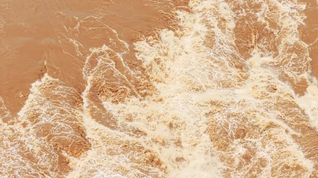 Powerful muddy river rapids surge and churn with white foam during a smooth pull back shot, capturing raw natural force, flood waters, and fluid dynamics for environmental and documentary edits.