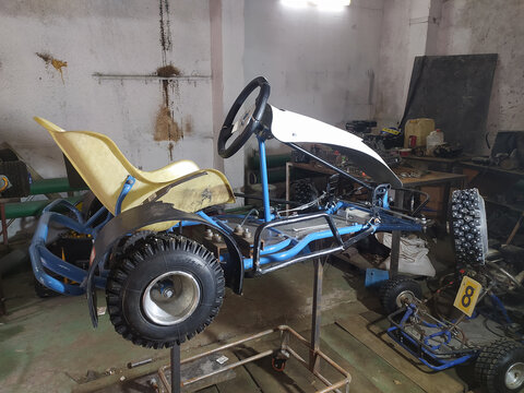 Blue racing kart being repaired in a garage. The go-kart sits on a repair table high off the ground. Engine removed,
