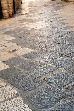 Wet cobblestone street pavement reflecting light with weathered stone blocks along a sidewalk