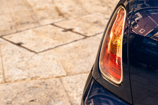 Rear taillight of a dark car parked on old cobblestone pavement in close up view