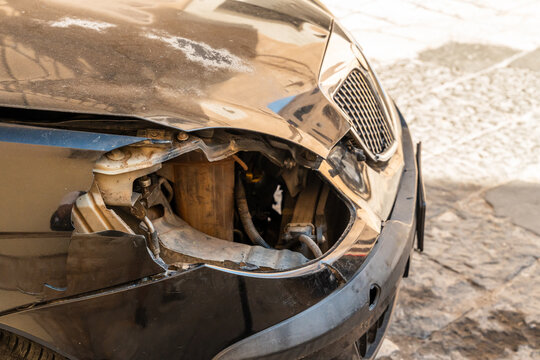Damaged front bumper of a car with broken headlight and crumpled metal parked on a stone street
