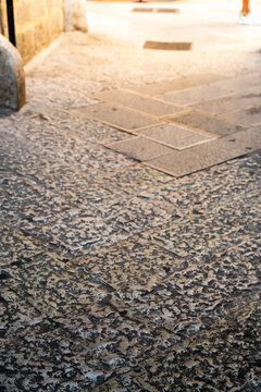Sunlit narrow alley with worn pebble stone pavement leading toward an illuminated doorway