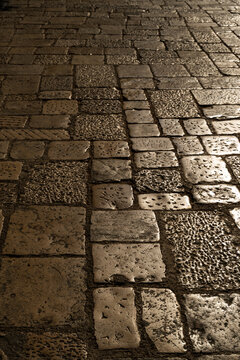 Vertical view of weathered cobblestone pavement with dark and light stone blocks in sunlight