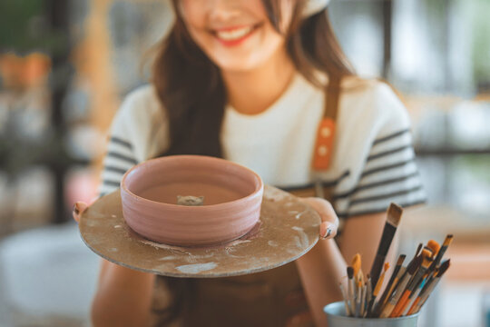 Happy female potter presenting handmade ceramic bowl in pottery studio, creative craftsmanship and small business artisan concept
