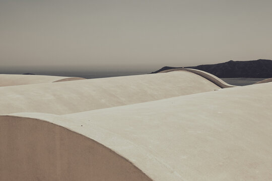 Smooth white curved rooftops stretch toward the distant horizon under hazy light, capturing minimalist architecture and the tranquil essence of Mediterranean design.