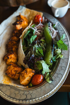Grilled chicken shish kebab served with roasted peppers and fresh salad on traditional metal plate.