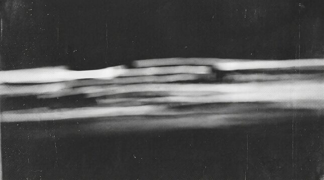 A blurry, horizontal, black and white photograph showing a long, indistinct object with layered segments against a dark background.