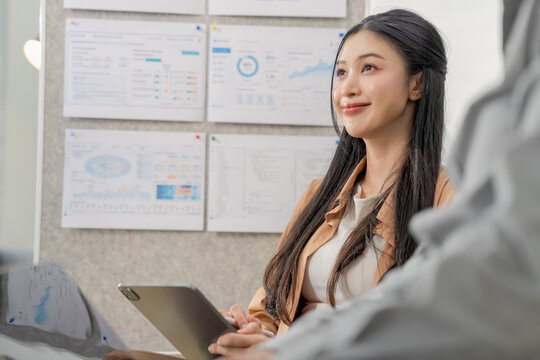 Young businesswoman listening attentively during meeting, holding digital tablet, thoughtful smile while colleague speaks, active listening and engagement in office discussion concept