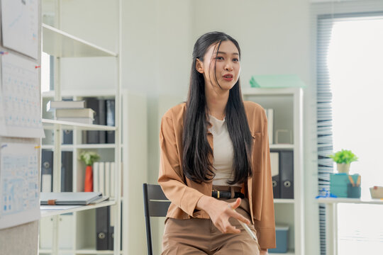 Confident businesswoman pointing at whiteboard chart, explaining strategy and presenting data during office meeting, close-up dynamic angle capturing leadership and business presentation concept