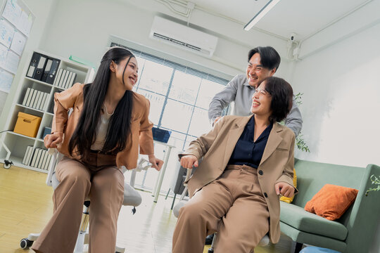 Three coworkers cheer triumphantly with raised fists, captured in a dynamic low angle in a bright office &mdash; an energetic celebration of team success, achievement, and workplace victory.