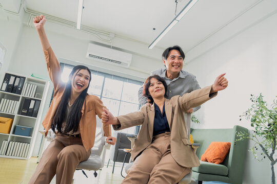 Three coworkers cheer triumphantly with raised fists, captured in a dynamic low angle in a bright office &mdash; an energetic celebration of team success, achievement, and workplace victory.