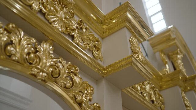 Luxurious gold gilded moldings with intricate baroque carvings against clean white walls. Soft natural lighting highlights metallic sheen depth