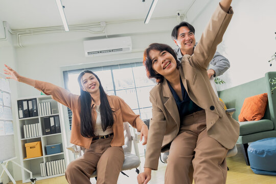Three coworkers cheer triumphantly with raised fists, captured in a dynamic low angle in a bright office &mdash; an energetic celebration of team success, achievement, and workplace victory.