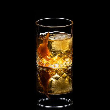 Close up of a classic old fashioned cocktail on a dark reflective background garnished with an orange twist.