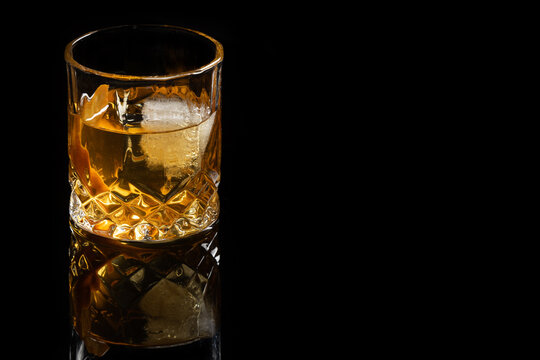 Close up of a classic old fashioned cocktail on a dark reflective background garnished with an orange twist.
