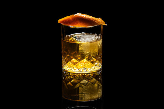 Close up of a classic old fashioned cocktail on a dark reflective background garnished with an orange twist.