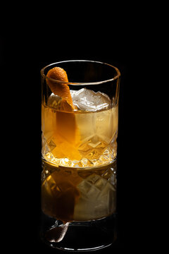Close up of a classic old fashioned cocktail on a dark reflective background garnished with an orange twist.