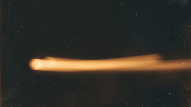 High-speed photograph capturing a luminous projectile in motion against a dark, featureless background, creating a streaking light effect.