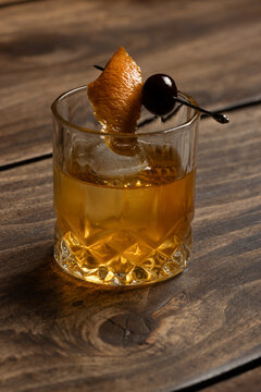 Close up of a classic old fashioned cocktail on a wooden background garnished with an orange twist and a cherry.