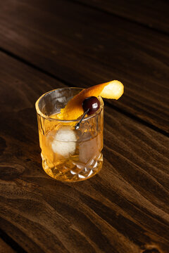 Close up of a classic old fashioned cocktail on a wooden background garnished with an orange twist and a cherry.
