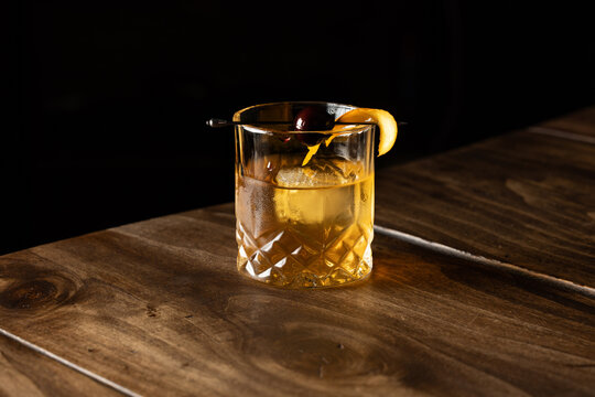 Close up of a classic old fashioned cocktail on a wooden background garnished with an orange twist and a cherry.
