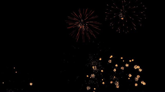 Bright sparks of fireworks in the night sky, purple and gold. Medium shot