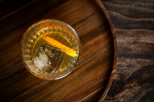 Close up of a classic old fashioned cocktail on a dark wooden background garnished with an orange twist.