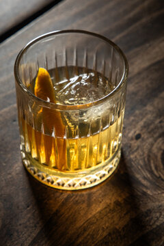 Close up of a classic old fashioned cocktail on a dark wooden background garnished with an orange twist.