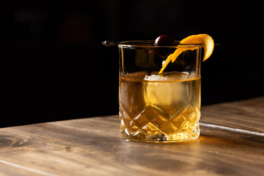 Close up of a classic old fashioned cocktail on a wooden background garnished with an orange twist and a cherry.