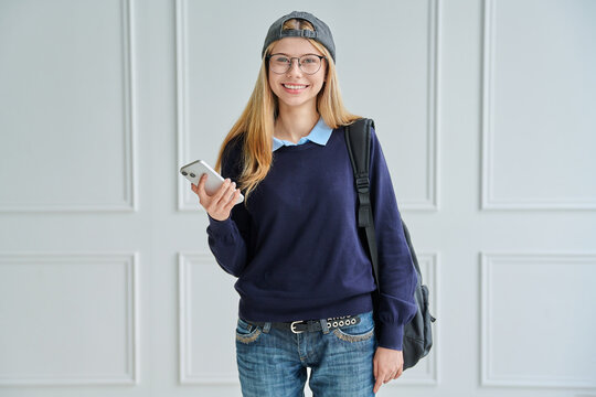 Smiling teenage student with backpack holding phone