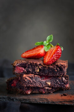 Close-up of a stack of chocolate brownies topped with a halved fresh strawberry on a slate board
