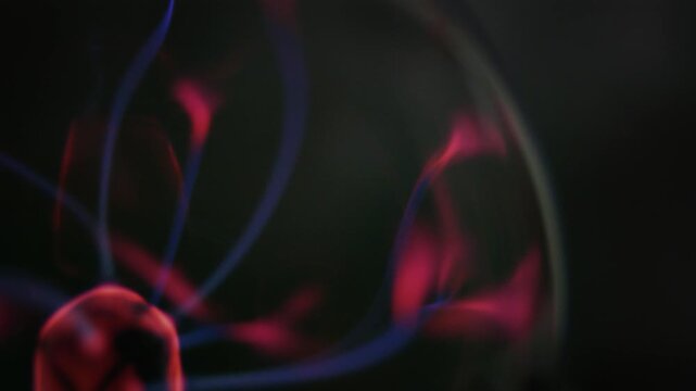 Detail of a plasma ball glowing, showing electric discharge and energy. Red and blue thunder light strands, on a dark background, macro shot, video loop