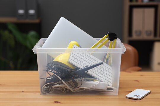 Recycling. Plastic container with different broken household appliances on wooden table indoors