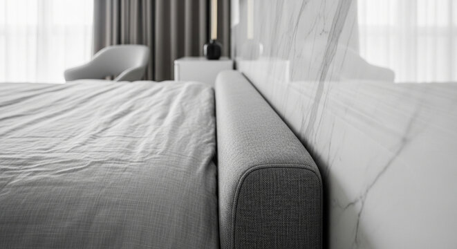 Close-up shot of a modern minimalist bed with a grey fabric headboard and neat bedding, set against a light marble wall in a contemporary bedroom interior.