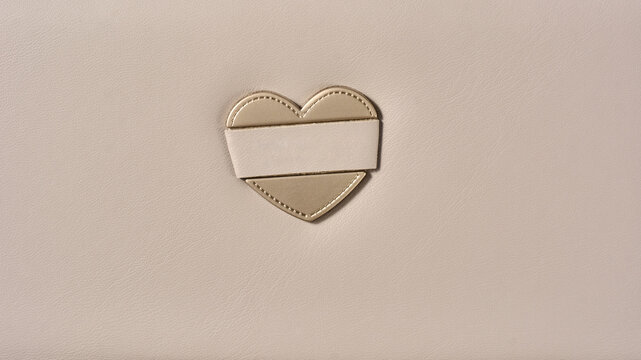 heart shaped metallic clasp on beige leather wallet, textured surface in close-up view with copy space, elegant fashion accessory background
