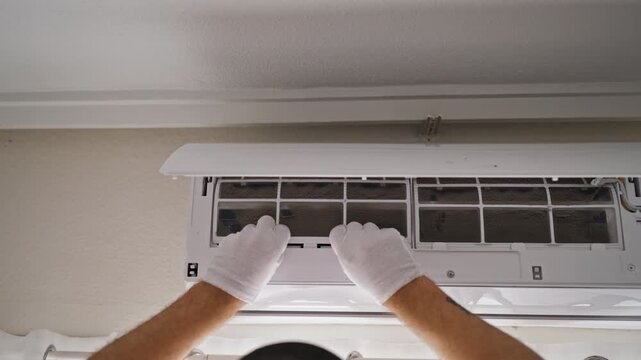Close-up of gloved HVAC technician examining an extremely dusty air conditioner filter and checking accumulated dirt by hand. Professional cleaning, hygiene and appliance care concept.