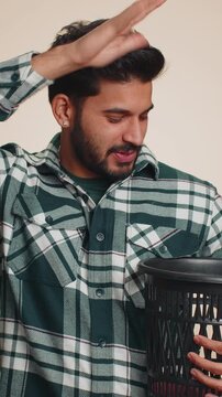Indian bearded man taking off throwing out glasses into bin after medical vision laser treatment therapy surgery looking smiling at camera. Handsome Hindu boy isolated alone on beige studio background