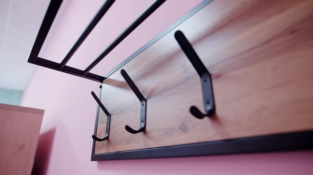 Wall-mounted coat rack features metal shelf frame and wooden backboard. Sturdy metal hooks offer practical hanging storage on pink wall