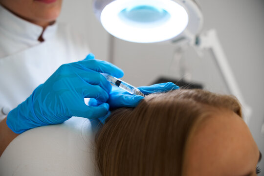 Specialist trichologist administering medicine into a patient scalp helping to combat baldness and stimulate new follicle growth.