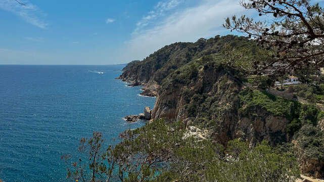 serene aerial view of the mediterranean sea with rocky cliffs and lush vegetation, showcasing the natural beauty of the coastline with vibrant blue and green waters and white clouds.