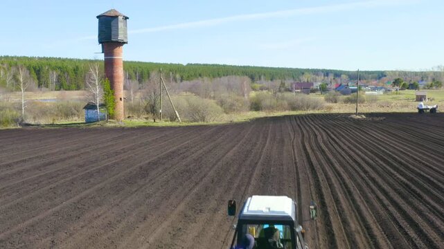 Russia, the Urals. Planting potatoes on the field with a combine and tractor. Spring. Drone footage